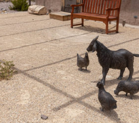 Realistic statues of a goat and chickens outside of an old building.
